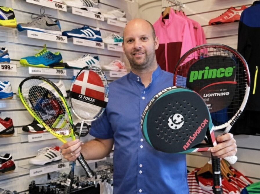 Ejeren Torben, står i den fysiske butik, med padelbat, tennisketcher og badmintonketchere i hånden